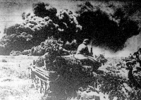Gépkocsizó-lövészek előnyomulása egy olajvidéken. A háttérben felgyújtott olajtartály füstcsóvája száll a magasba.