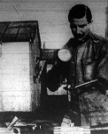 A félkaru rokkant vésni is tud. Bal műkarja fogó-készülékben végződik. Erre van rásrófolva a véső. Jobb kezében tartja a vastag fakalapácsot és ezzel veri be a a vésőt a gyalupadra erősített fába.