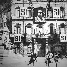 A fasiszta párt főhadiszállása. Óriási méretű  arcképe a Ducének, hatalmas plakátok és SI, azaz Igen jelszó.